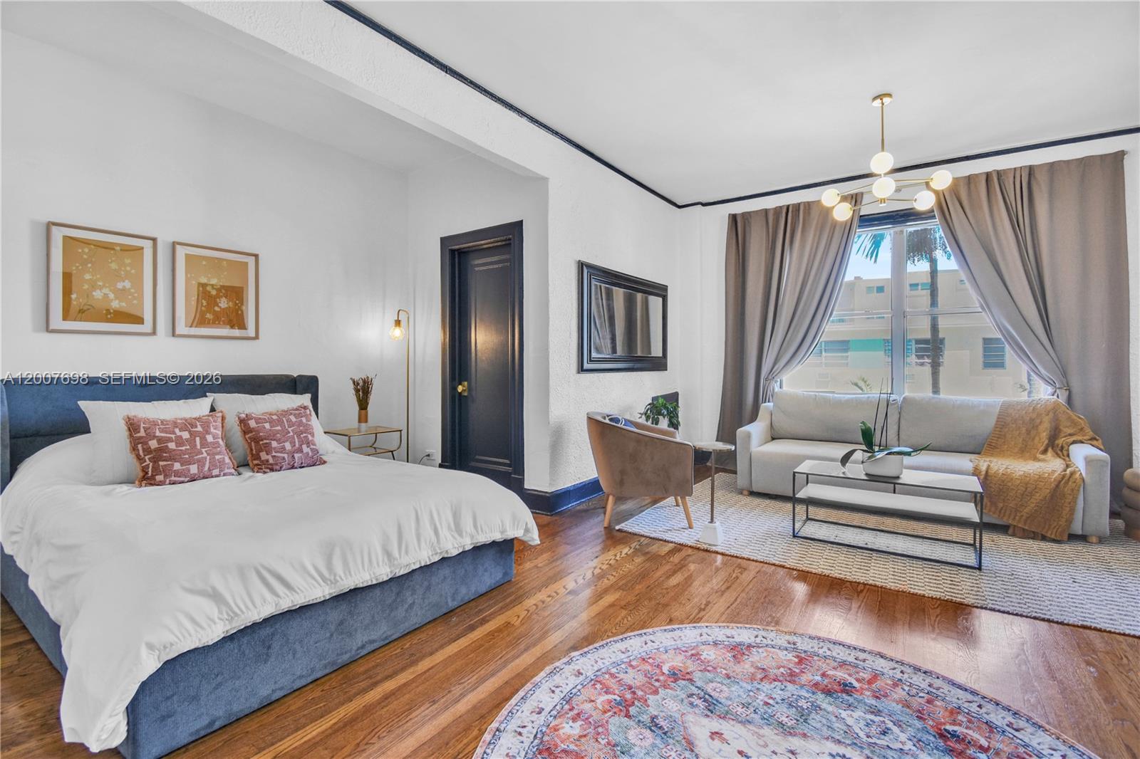 A bedroom with a bed, seating area, hardwood floors, and a dark-painted door — 900 16th St # 201, Miami Beach FL 33139, MIAMI BEACH, FL