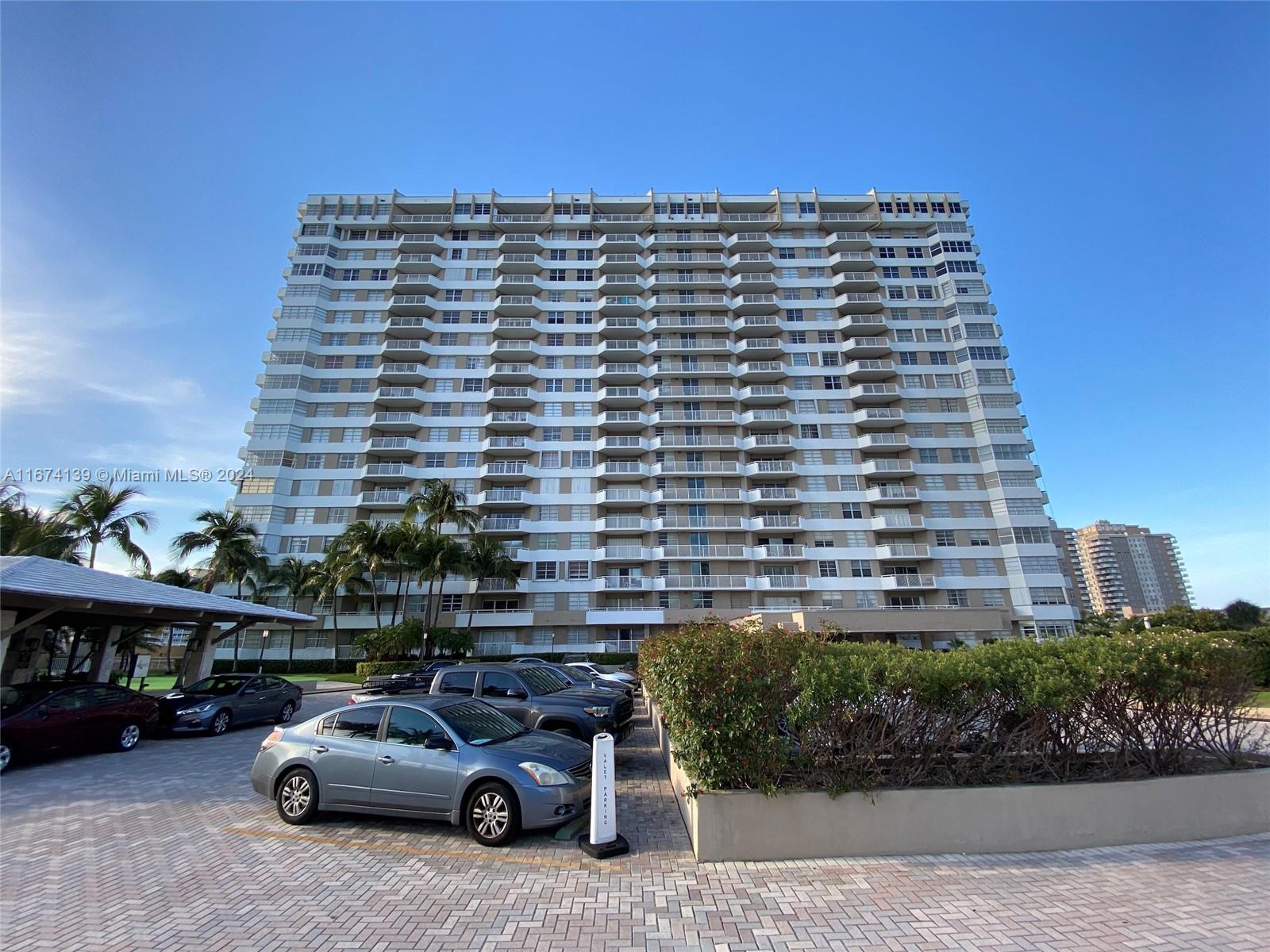A multi-story residential apartment building stands behind a parking lot with several parked cars — 1965 S Ocean Dr # 4D, Hallandale Beach FL 33009, HALLANDALE BEACH, FL