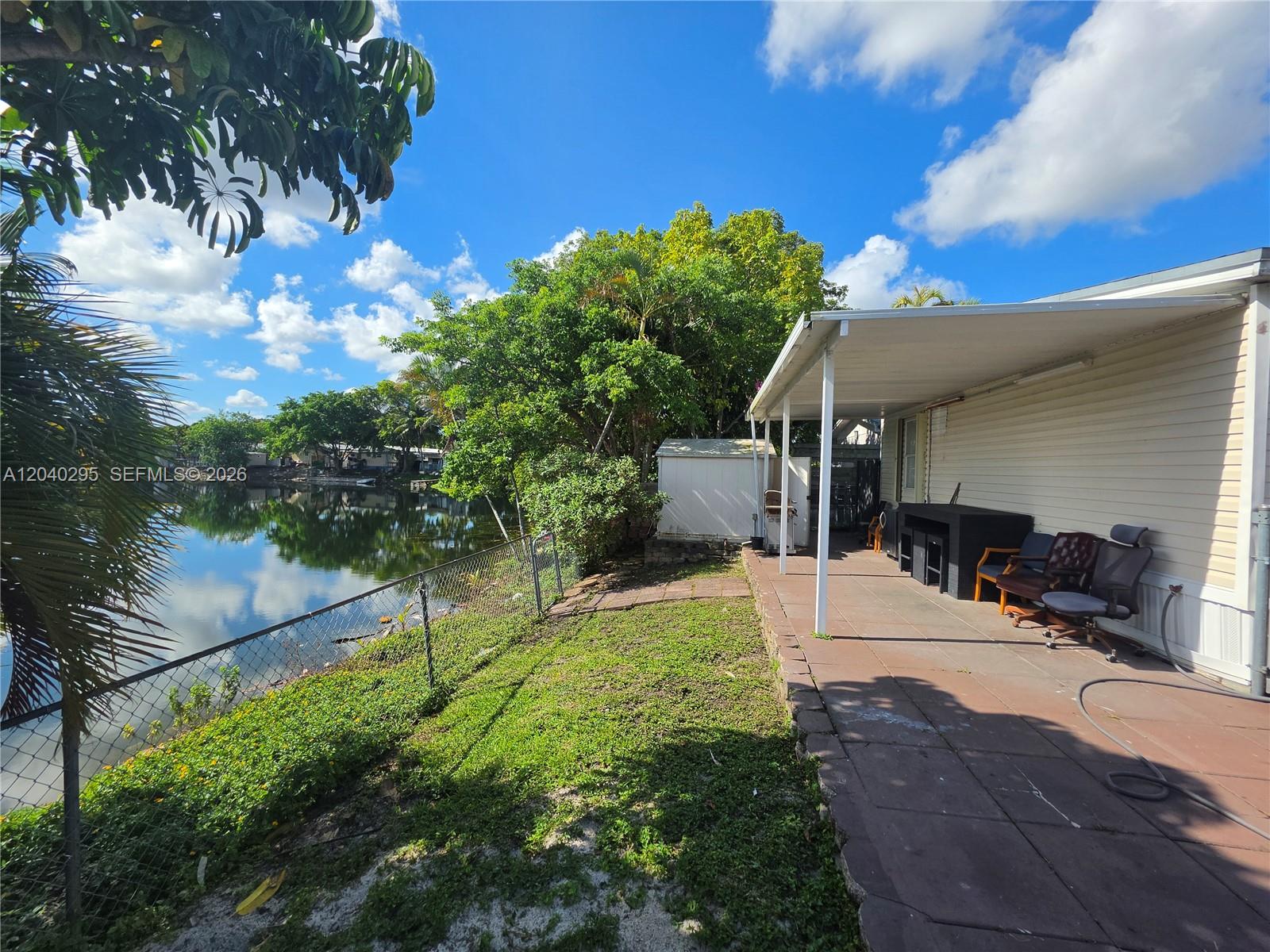 A paved patio with a covered roof overlooks a small lake and a grassy yard — 1529 SW 131 Avenue, Miami FL 33184, MIAMI, FL