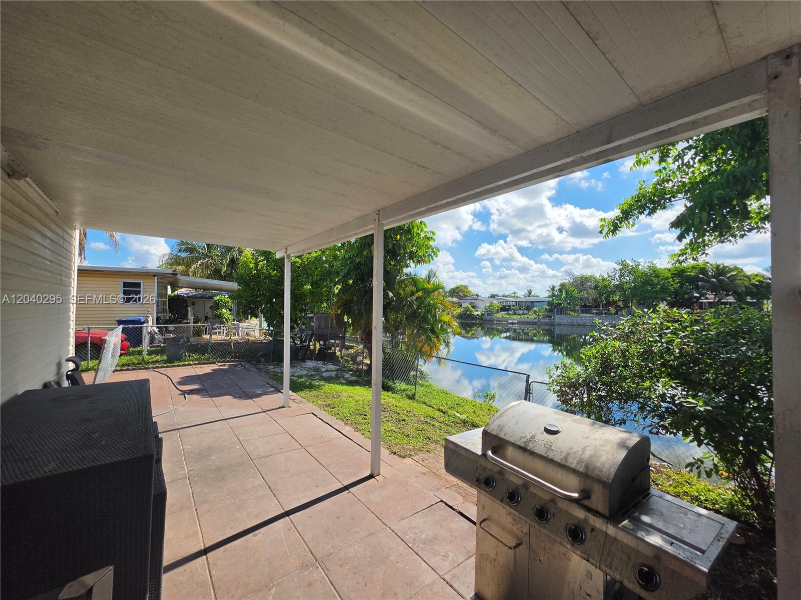 A covered patio overlooks a canal with a grill in the foreground — 1529 SW 131 Avenue, Miami FL 33184, MIAMI, FL