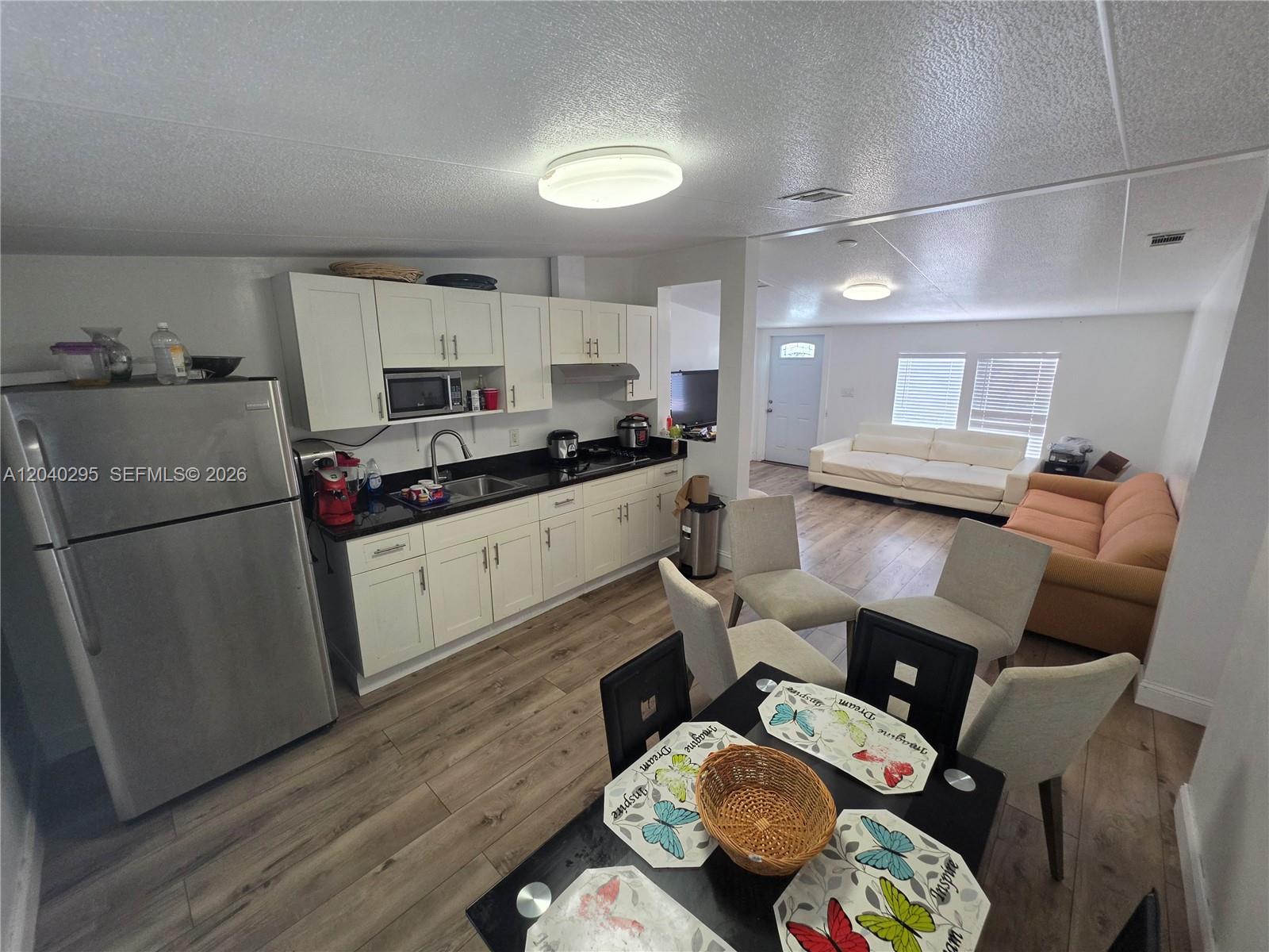 An open-concept kitchen and dining area features white cabinets, stainless appliances, and wood-look flooring — 1529 SW 131 Avenue, Miami FL 33184, MIAMI, FL