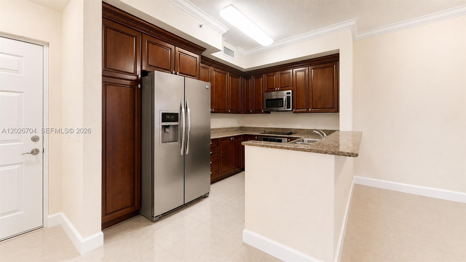 A kitchen features dark wood cabinets, stainless steel appliances, and a granite countertop peninsula — 4106 Renaissance Way # 106, Boynton Beach FL 33426, BOYNTON BEACH, FL