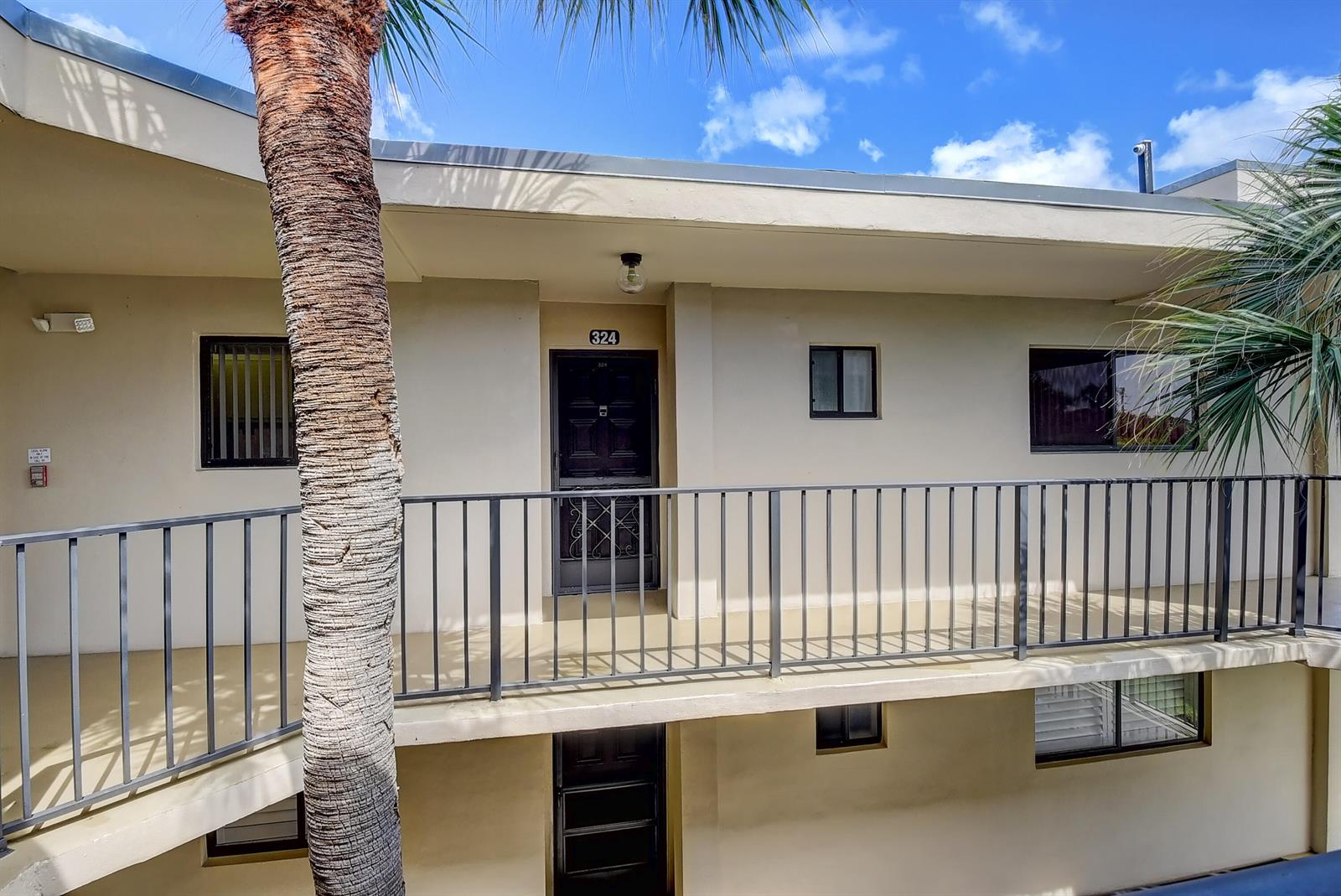 An exterior view of a two-story apartment building with a palm tree and metal railings — 5370 Las Verdes Circle # 324, Delray Beach FL 33484, DELRAY BEACH, FL