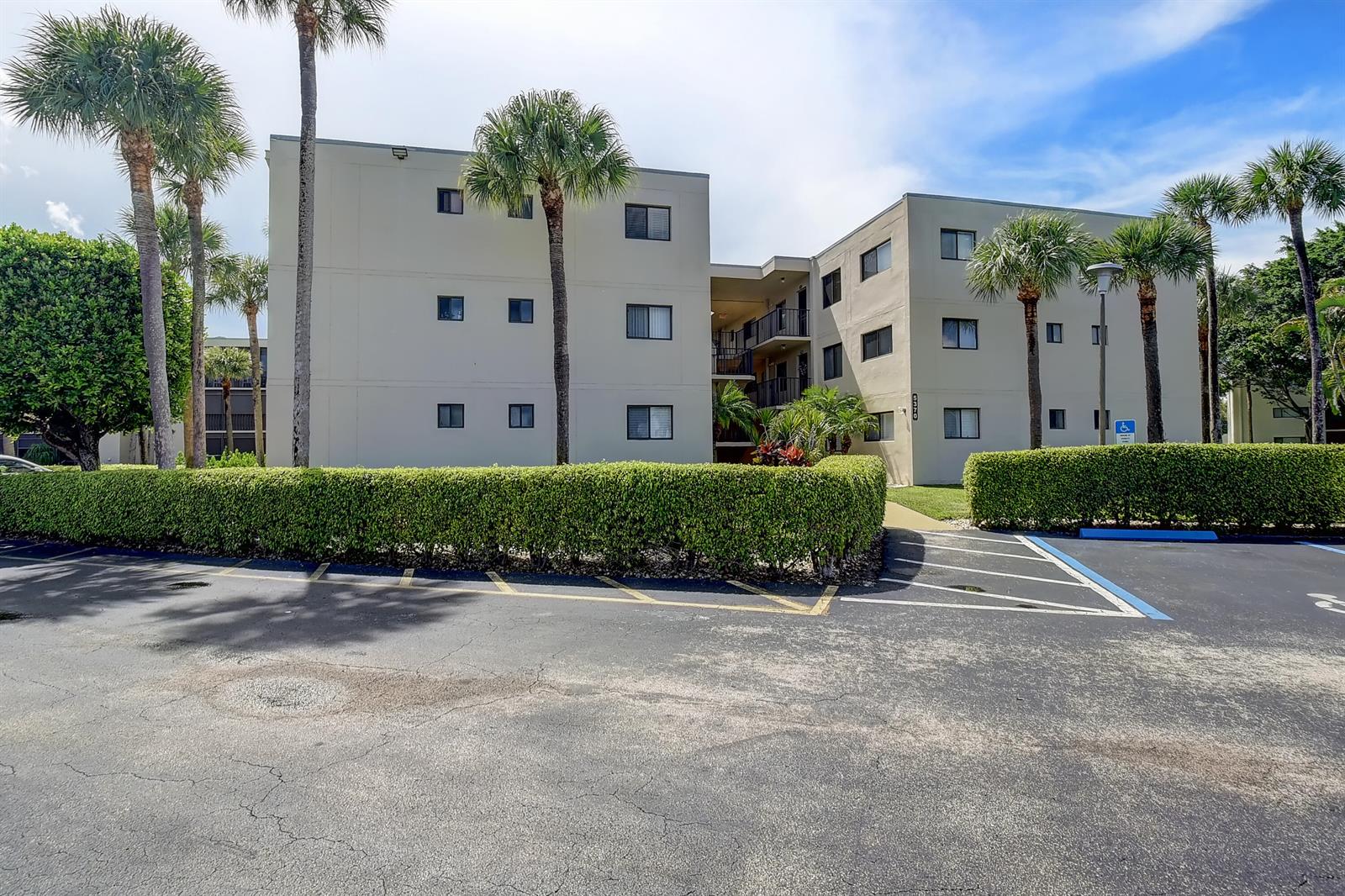 A three-story apartment building stands behind a manicured hedge and a paved parking lot — 5370 Las Verdes Circle # 324, Delray Beach FL 33484, DELRAY BEACH, FL