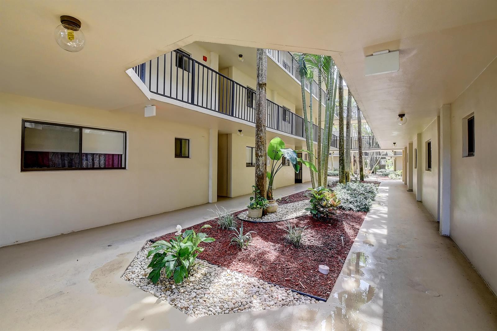 An open-air courtyard with a central garden bed surrounded by a multi-story apartment building — 5370 Las Verdes Circle # 324, Delray Beach FL 33484, DELRAY BEACH, FL