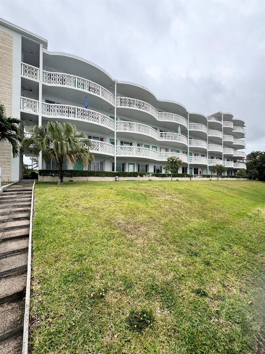 A multi-story apartment building with curved balconies and a grassy lawn in the foreground — 2381 Sunset Avenue # 117, FL 33461, FL