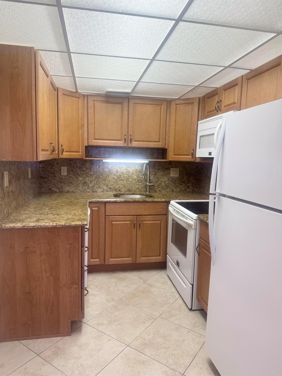 A kitchen features wood cabinets, granite countertops, a white refrigerator, and a drop ceiling — 2381 Sunset Avenue # 117, FL 33461, FL