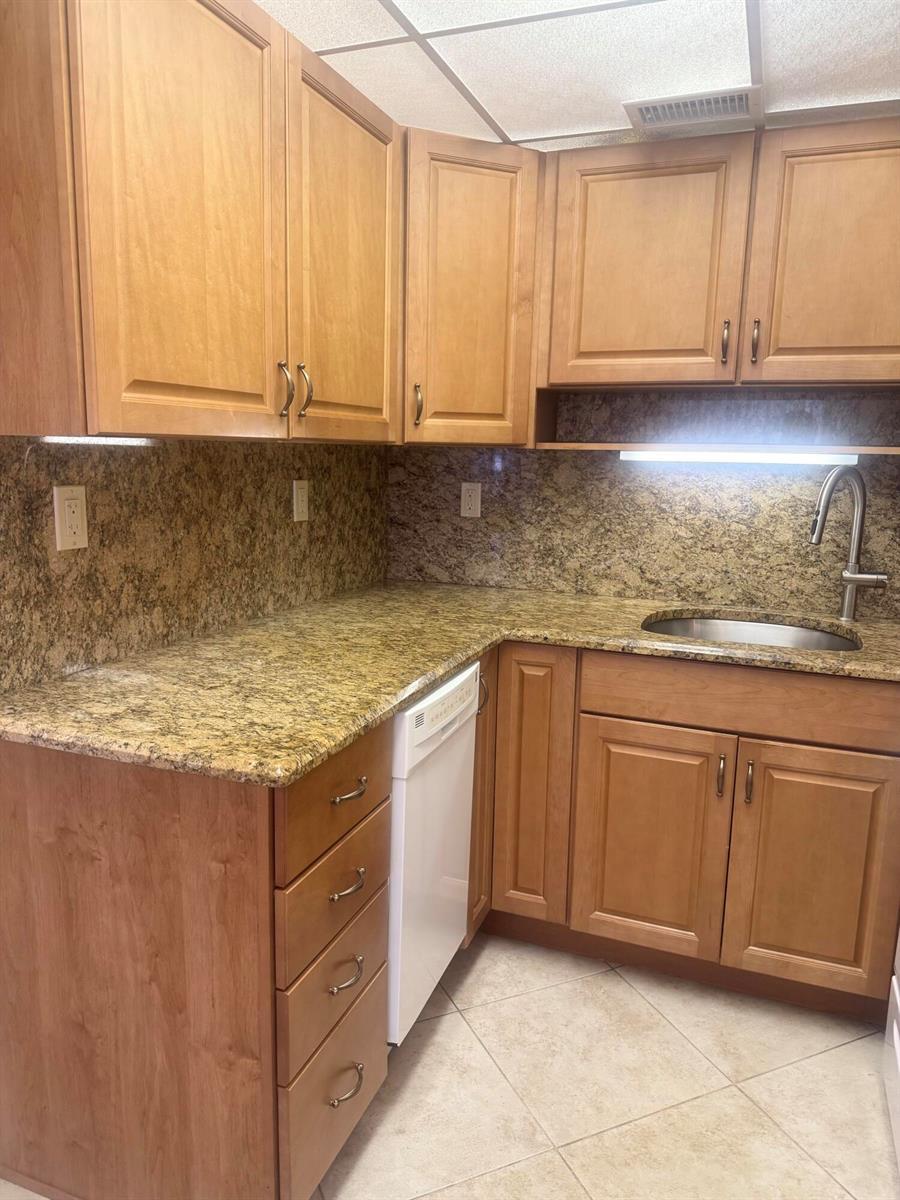 A kitchen features light wood cabinets, granite countertops, a white dishwasher, and a stainless sink — 2381 Sunset Avenue # 117, FL 33461, FL