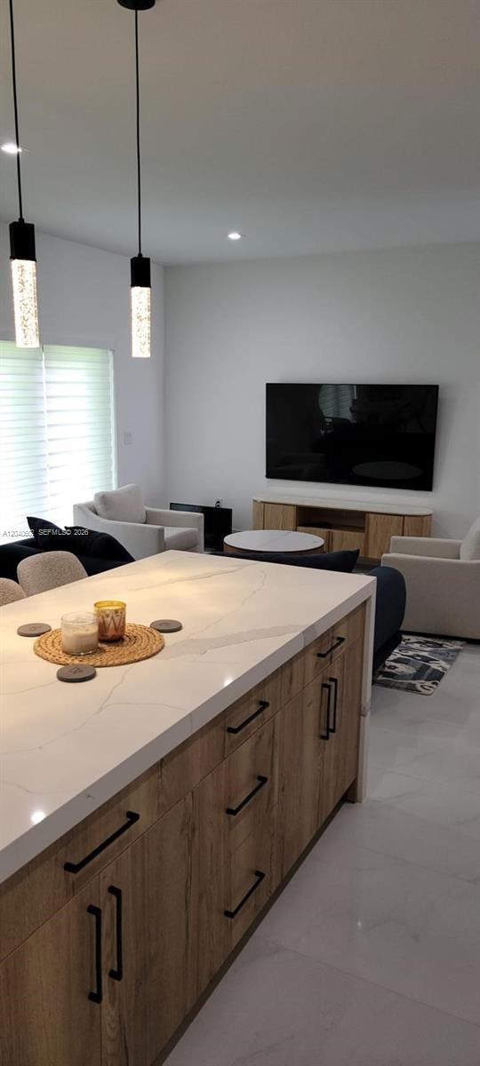 A kitchen island with a white marble countertop overlooks a living room with a television — 5901 SW 64th St, South Miami FL 33143, SOUTH MIAMI, FL