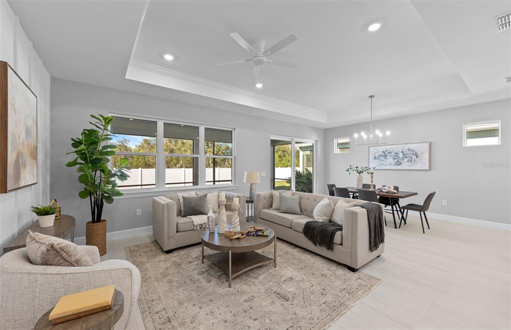 A bright open-concept living and dining area with light tile floors and a tray ceiling — 1832 SILVER SHORES BOULEVARD, ENGLEWOOD, FL
