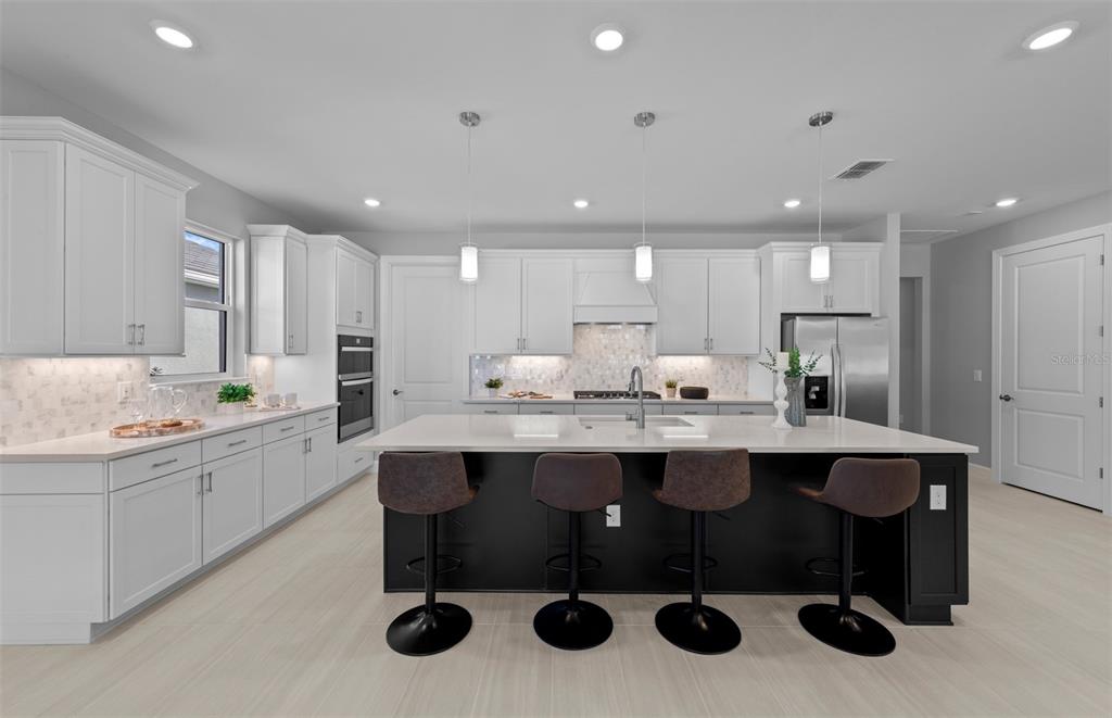 A modern kitchen features white cabinetry, a black island with bar stools, and stainless appliances — 1832 SILVER SHORES BOULEVARD, ENGLEWOOD, FL
