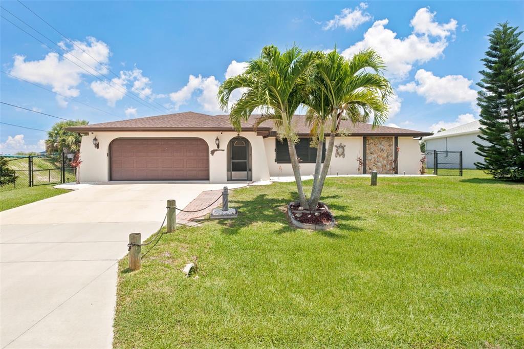 A single-story house with a brown garage door, a palm tree, and a grassy lawn — 18881 MCGRATH CIRCLE, PORT CHARLOTTE, FL