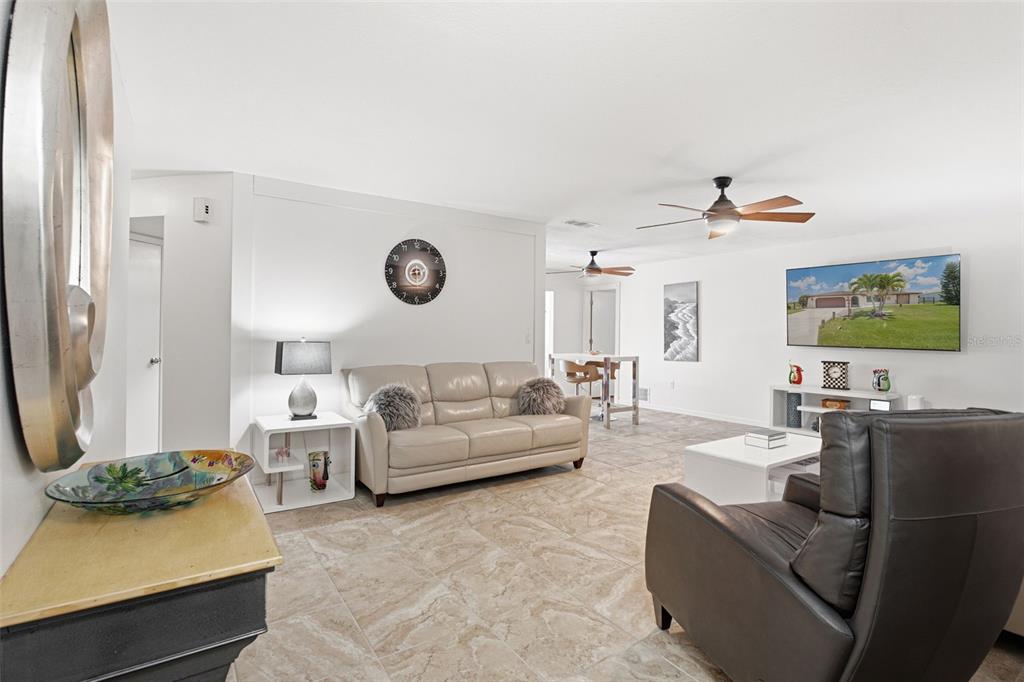 A living room features light-colored tile flooring, a beige sofa, and a wall-mounted television — 18881 MCGRATH CIRCLE, PORT CHARLOTTE, FL