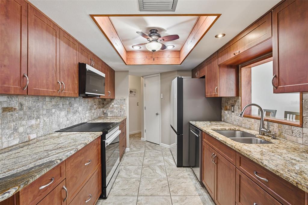 A galley kitchen features wood cabinets, granite countertops, stone tile backsplash, and a tray ceiling — 18881 MCGRATH CIRCLE, PORT CHARLOTTE, FL