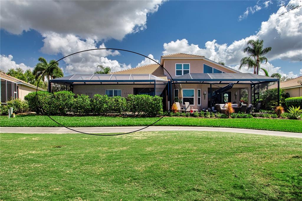 The rear exterior of a house features a large screened-in patio and landscaped hedges — 9448 FOREST HILLS CIRCLE, SARASOTA, FL