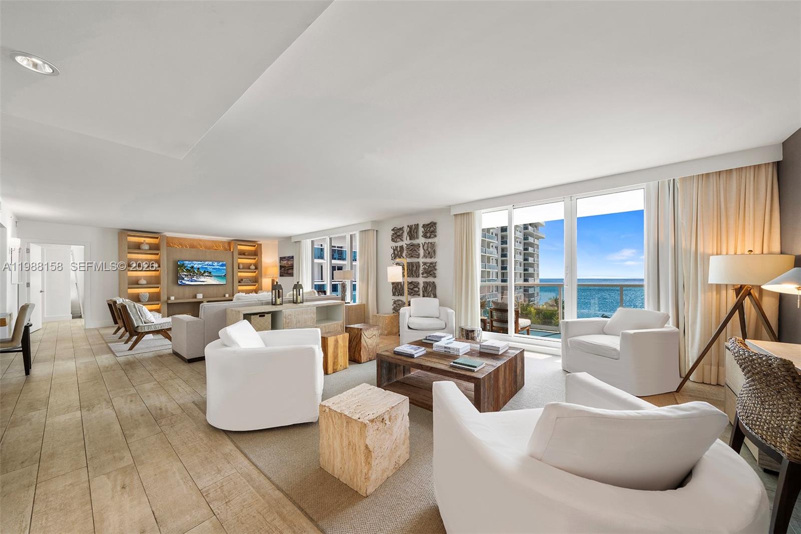 A bright, modern living room features white armchairs, a wooden coffee table, and ocean views — 102 24th St # 1040, Miami Beach FL 33139, MIAMI BEACH, FL