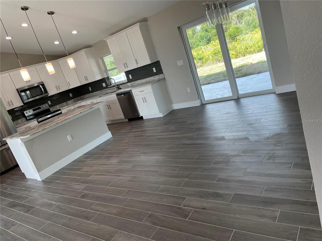 A kitchen with white cabinets, dark countertops, and wood-look tile flooring opens to a patio — 00 LONGFELLOW LANE, NORTH PORT, FL
