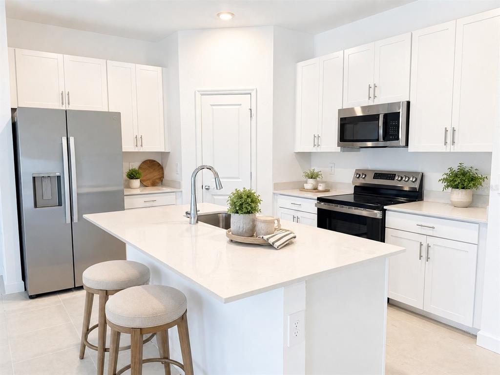 A modern kitchen features white cabinets, stainless steel appliances, a quartz island, and bar stools — 8206 SAINT KITTS CIRCLE, ENGLEWOOD, FL