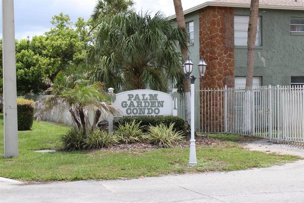 A sign for Palm Garden Condo stands in front of a building with stone accents — 703 MICHIGAN COURT UNIT 2, ST CLOUD, FL