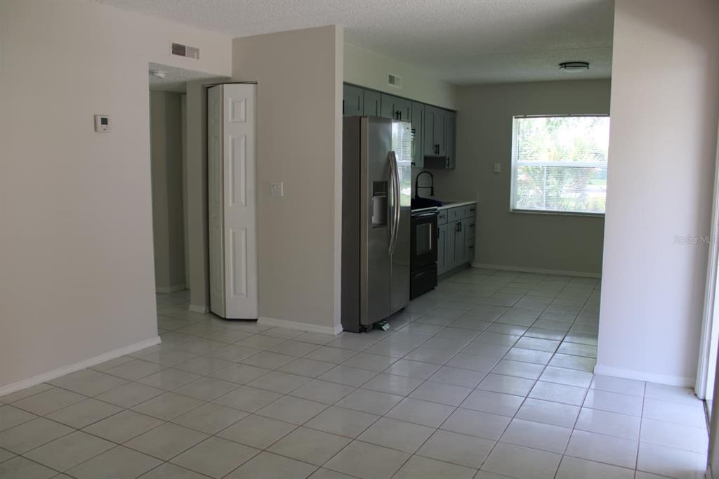 A kitchen with gray cabinets and stainless steel appliances opens to a tiled dining area — 703 MICHIGAN COURT UNIT 2, ST CLOUD, FL