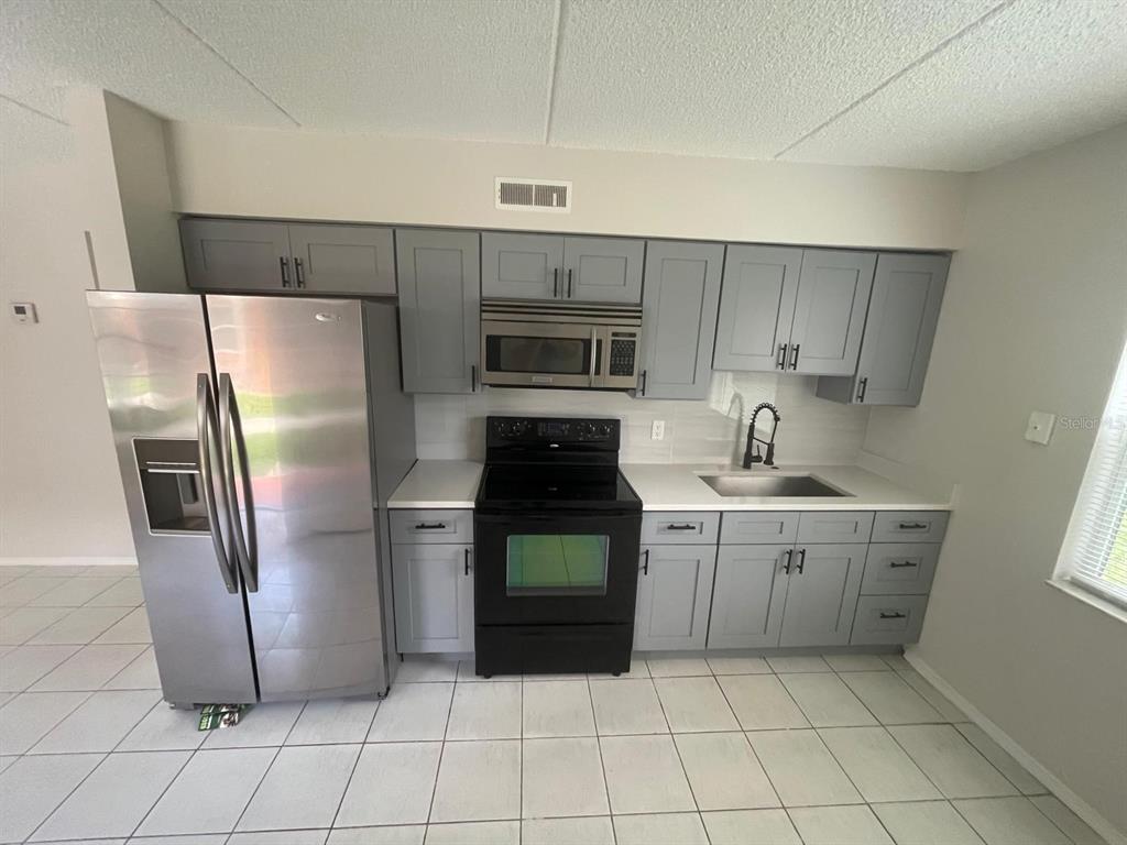 A kitchen features gray cabinets, stainless steel appliances, a black stove, and white tile flooring — 703 MICHIGAN COURT UNIT 2, ST CLOUD, FL