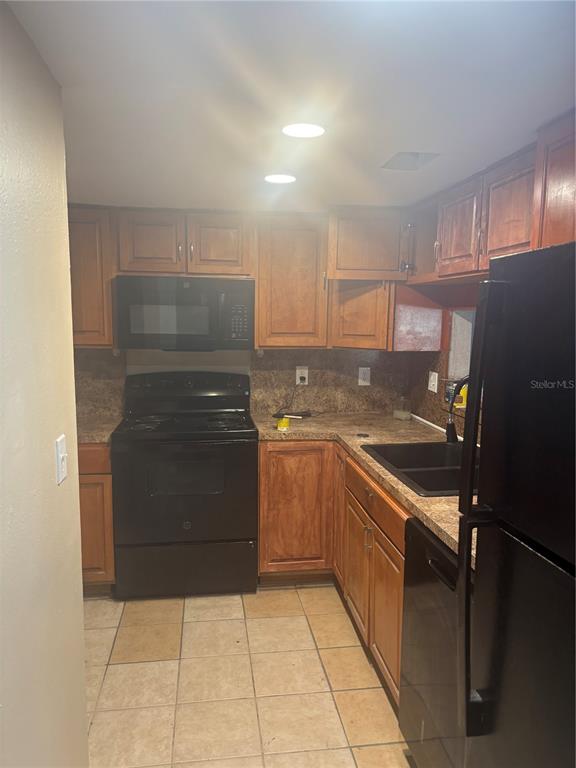 A kitchen features wood cabinets, black appliances, laminate countertops, and light-colored tile flooring — 1320 MOUNTAINVIEW UNIT 1320, TAMPA, FL