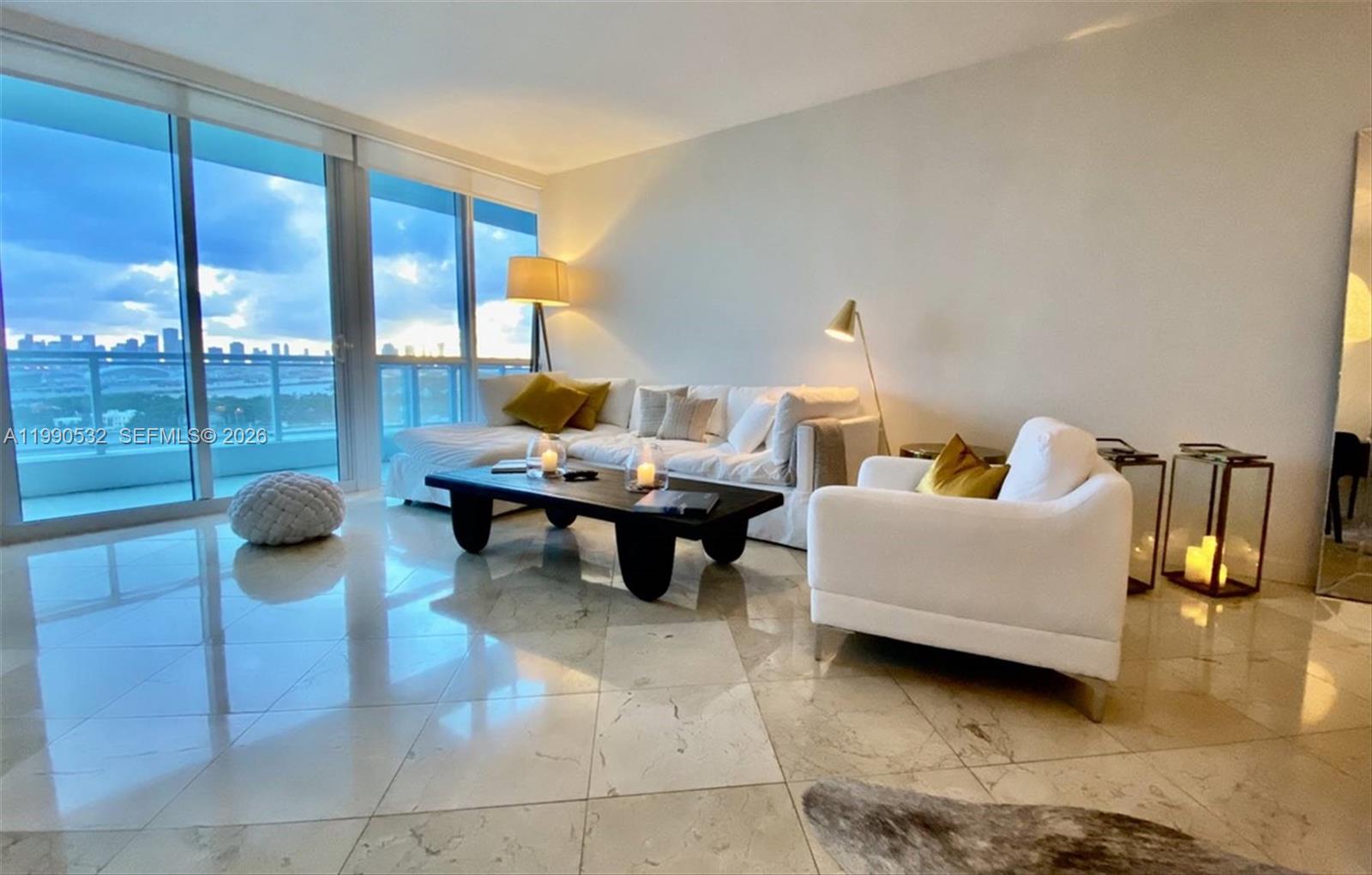A modern living room features a white sofa, dark coffee table, and floor-to-ceiling windows — 540 West Ave # 2011, Miami Beach FL 33139, MIAMI BEACH, FL
