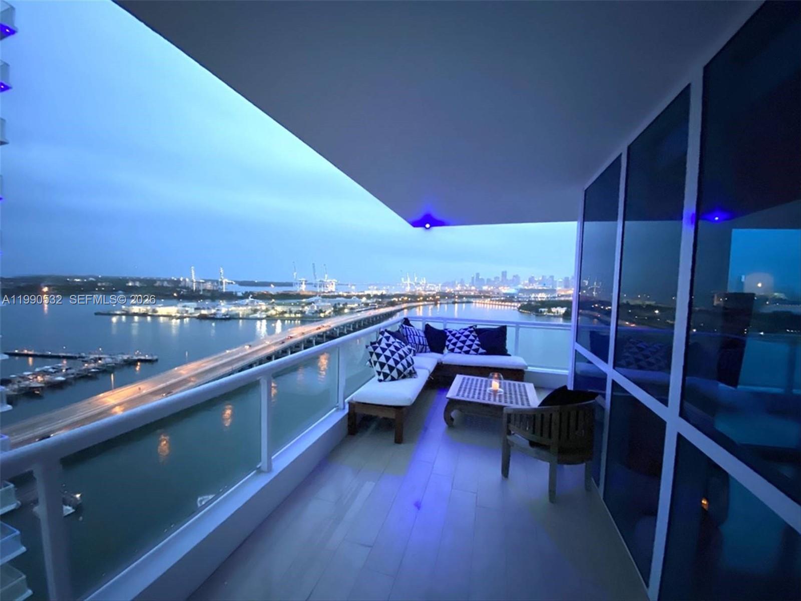 A balcony with outdoor seating overlooks a bridge, water, and a distant city skyline — 540 West Ave # 2011, Miami Beach FL 33139, MIAMI BEACH, FL