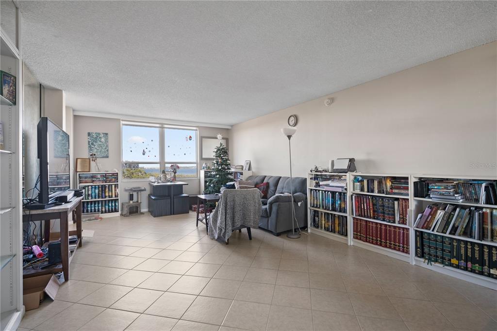 A living room with tile flooring, a gray sofa, bookshelves, and a window with water views — 2621 COVE CAY DRIVE UNIT 804, CLEARWATER, FL