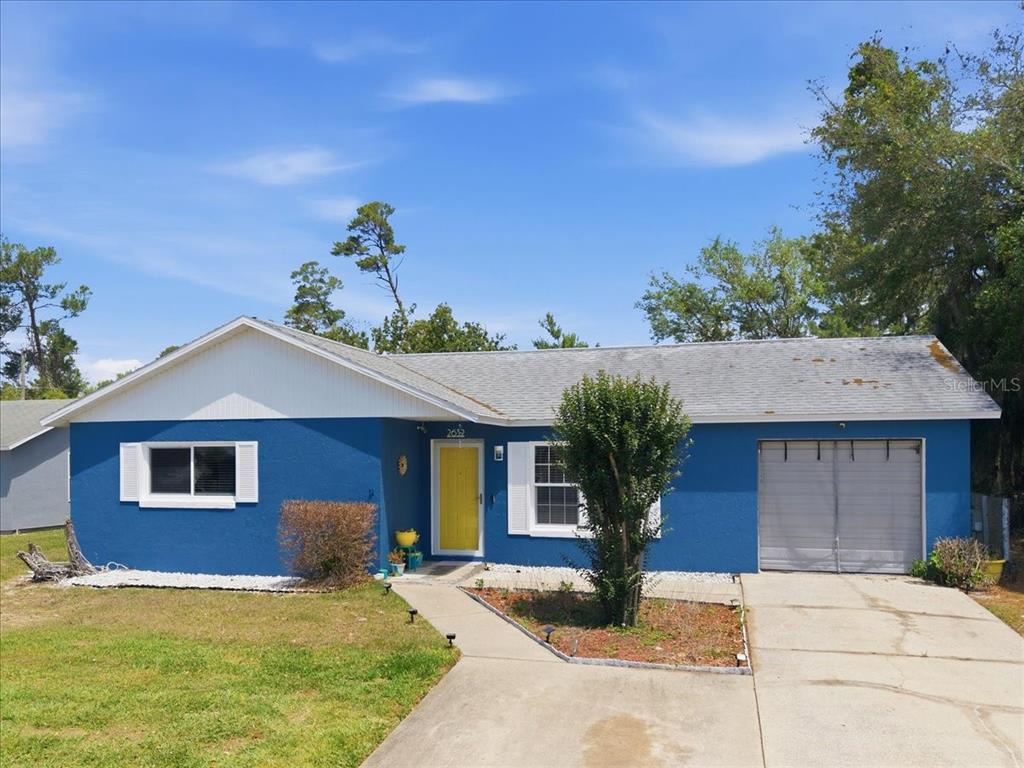 A single-story blue house with a white roof, yellow front door, and attached garage — 2632 DERBY DRIVE, DELTONA, FL