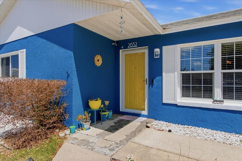 A bright blue house exterior features a yellow front door and a concrete walkway — 2632 DERBY DRIVE, DELTONA, FL