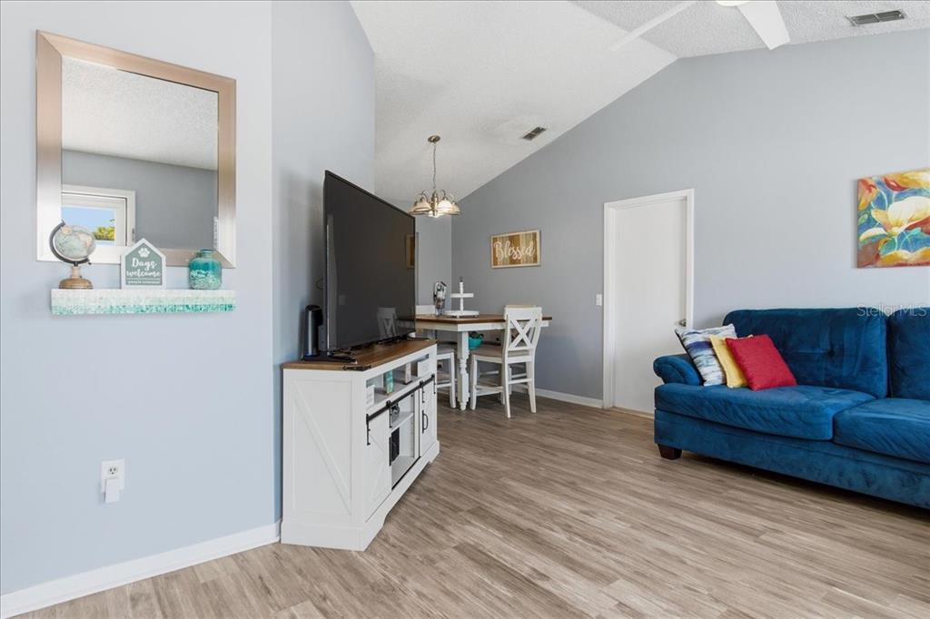 A living room features a blue sofa, a television on a white stand, and a dining area — 2632 DERBY DRIVE, DELTONA, FL