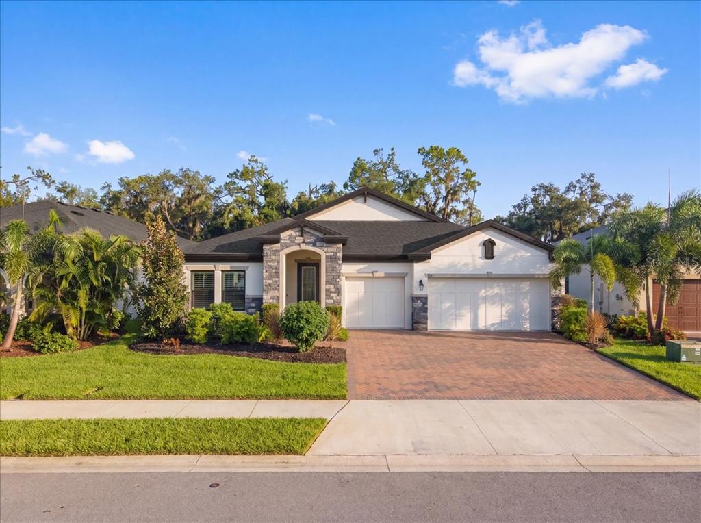 A single-story house with a stone-accented entryway, white stucco walls, and a brick paver driveway — 9145 WARM SPRINGS CIRCLE, PARRISH, FL