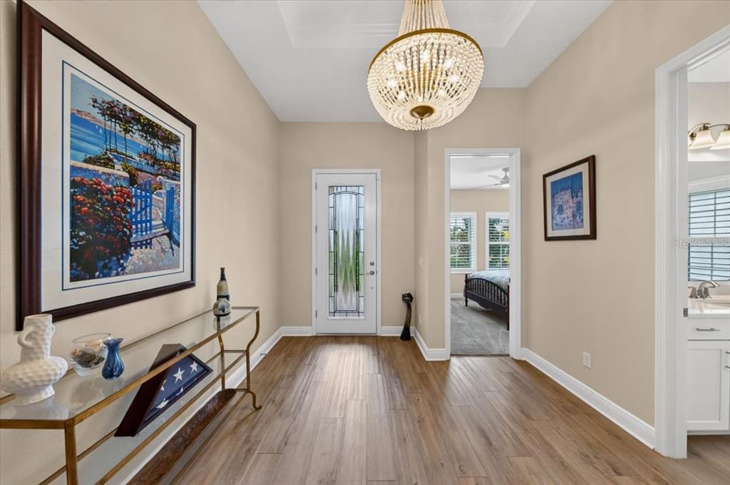 A foyer with wood-look flooring, a crystal chandelier, a glass console table, and a front door — 9145 WARM SPRINGS CIRCLE, PARRISH, FL