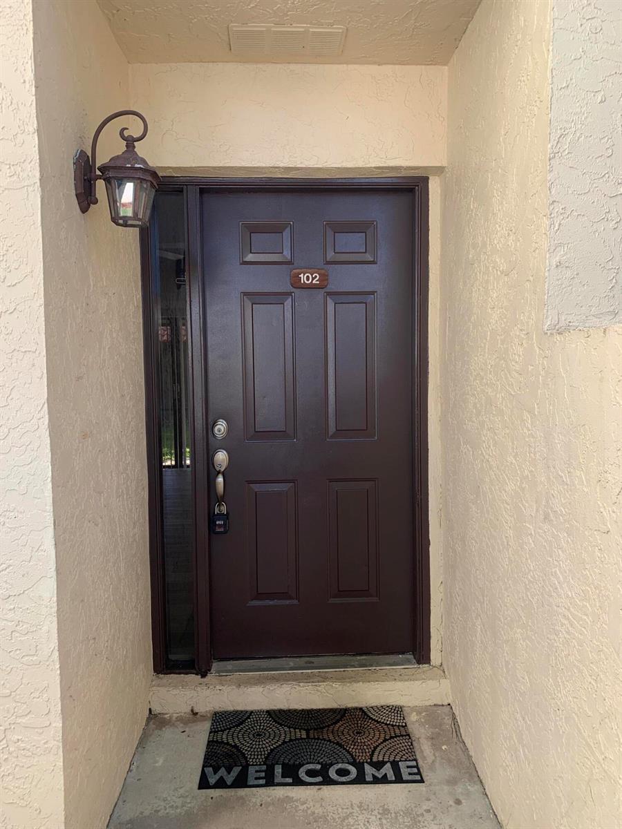 A dark brown front door with the number 102 and a welcome mat — 12 Via De Casas Sur # 102, Boynton Beach FL 33426, BOYNTON BEACH, FL