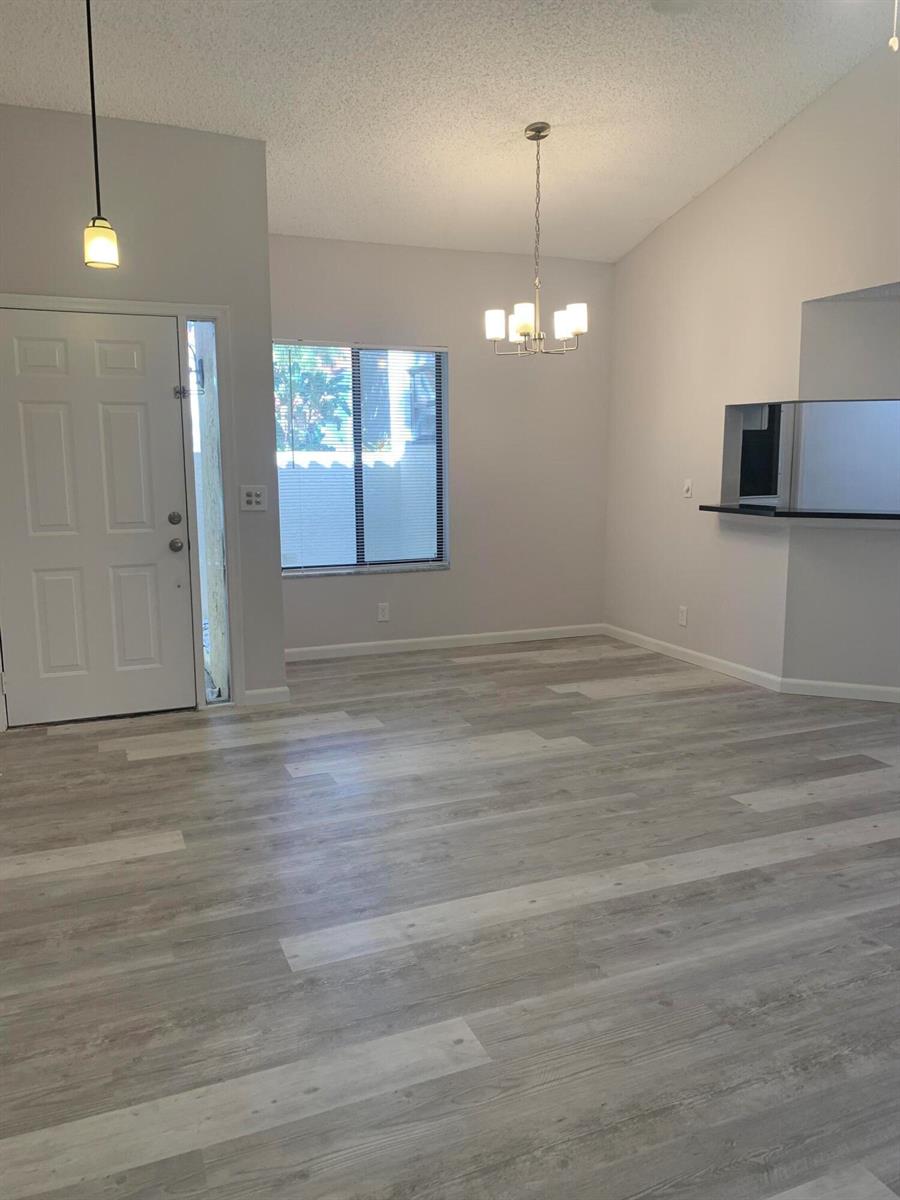 An empty room with light gray wood-look flooring, a white front door, and a chandelier — 12 Via De Casas Sur # 102, Boynton Beach FL 33426, BOYNTON BEACH, FL