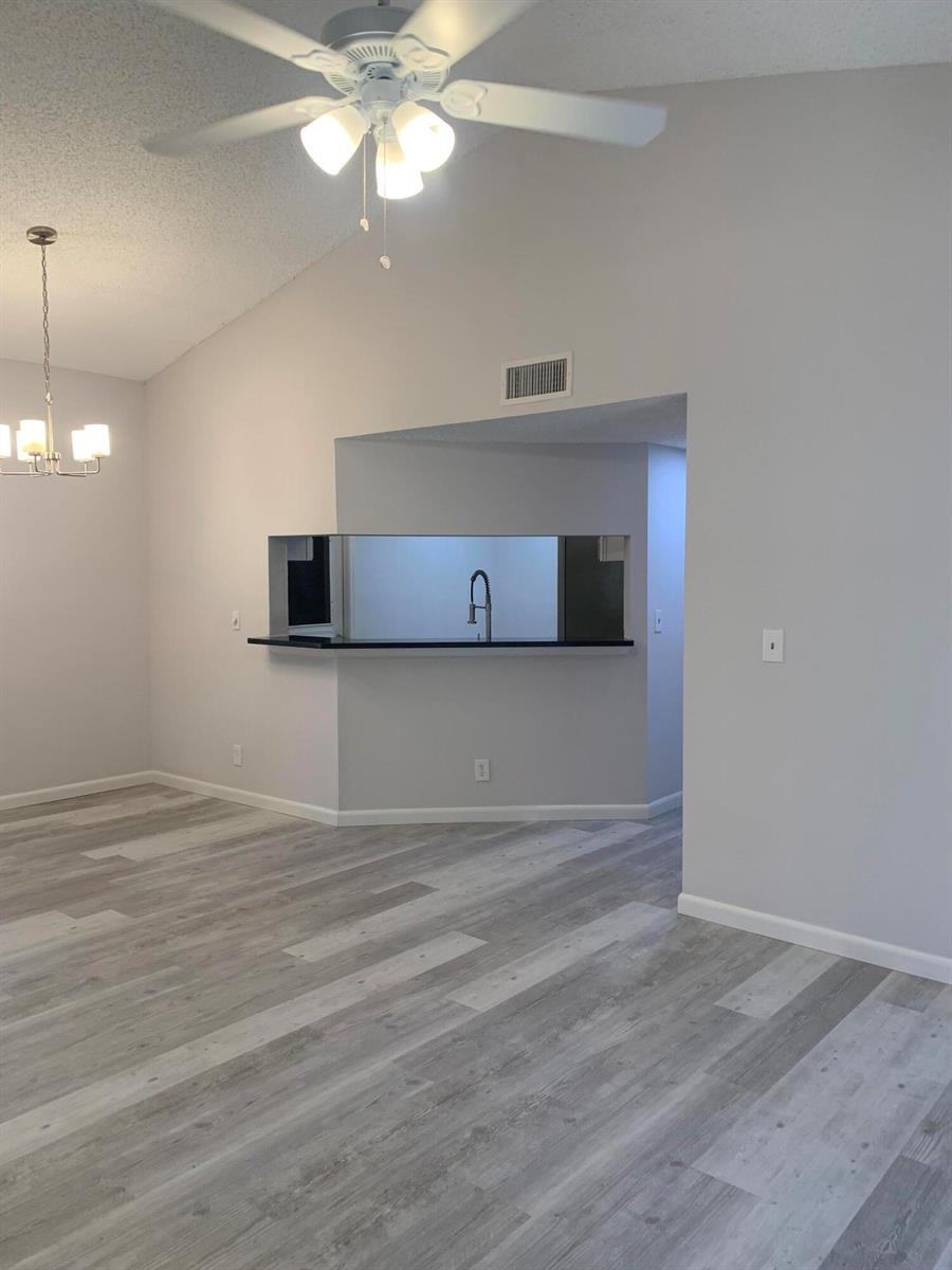 A living area with light gray wood-look flooring, a ceiling fan, and a kitchen pass-through — 12 Via De Casas Sur # 102, Boynton Beach FL 33426, BOYNTON BEACH, FL