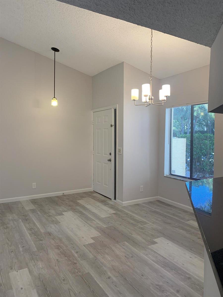 A dining area features light wood-look flooring, a chandelier, a pendant light, and a door — 12 Via De Casas Sur # 102, Boynton Beach FL 33426, BOYNTON BEACH, FL