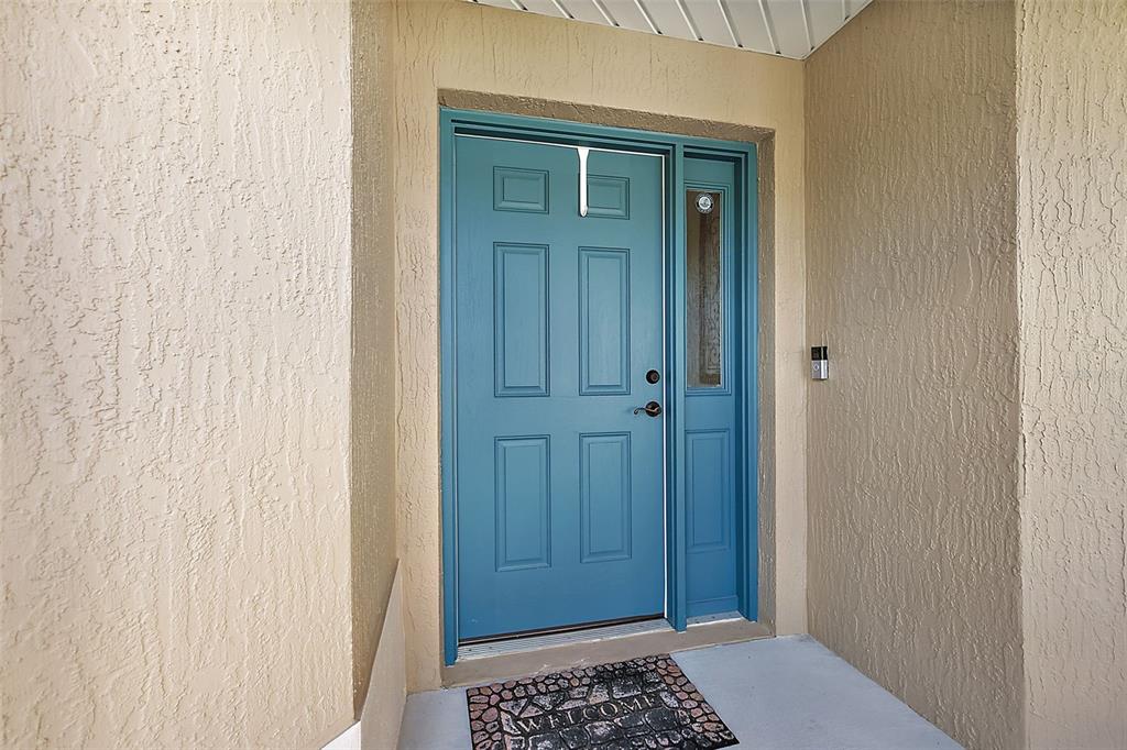 A blue front door with a side window is set into a beige stucco entryway — 1818 TRIMARCHE TERRACE, THE VILLAGES, FL