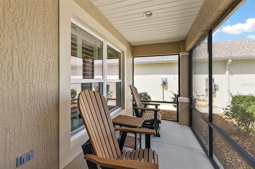 A screened-in porch features two wooden Adirondack chairs, a small side table, and concrete flooring — 1818 TRIMARCHE TERRACE, THE VILLAGES, FL