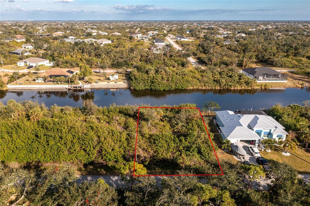 An aerial view shows a vacant, wooded residential lot outlined in red next to a house — 10168 COCOA BEACH STREET, PORT CHARLOTTE, FL