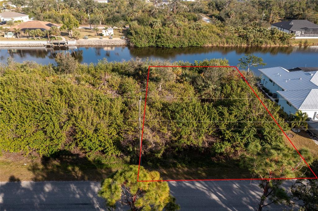 An aerial view shows a vacant, wooded residential lot outlined in red bordering a canal — 10168 COCOA BEACH STREET, PORT CHARLOTTE, FL