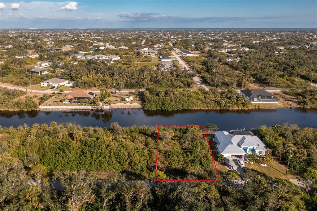 An aerial view shows a vacant, rectangular waterfront lot outlined in red next to a house — 10168 COCOA BEACH STREET, PORT CHARLOTTE, FL