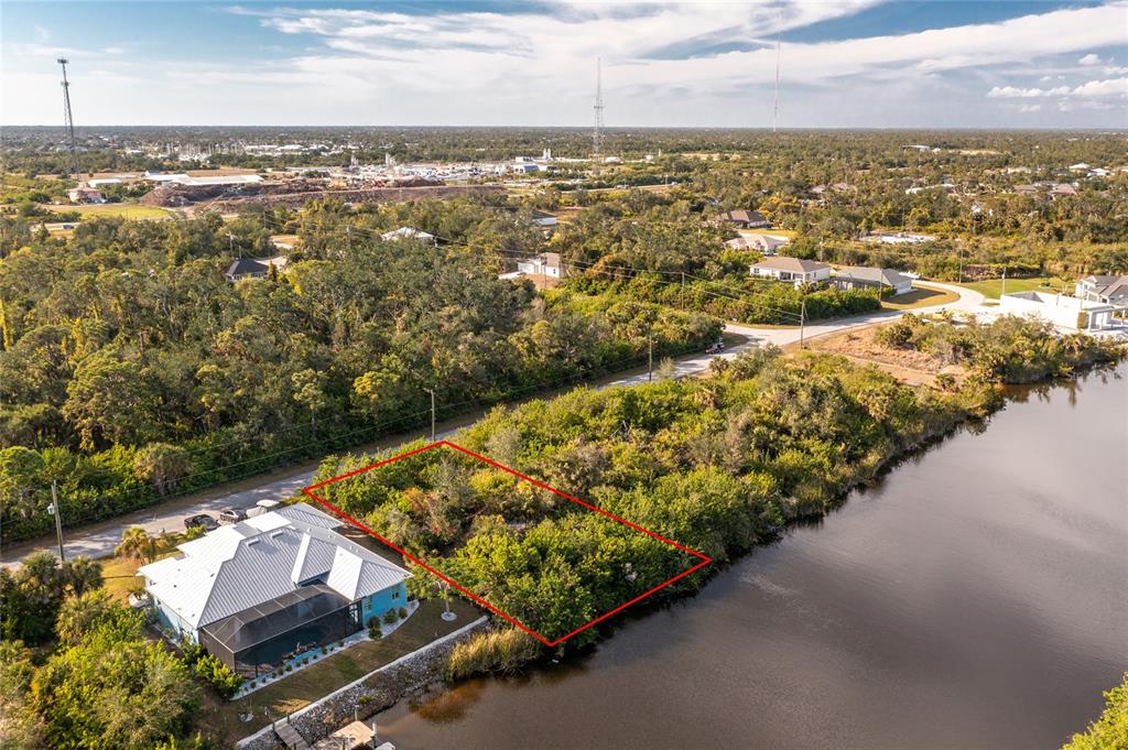 An aerial view shows a vacant, rectangular waterfront lot outlined in red next to a house — 10168 COCOA BEACH STREET, PORT CHARLOTTE, FL