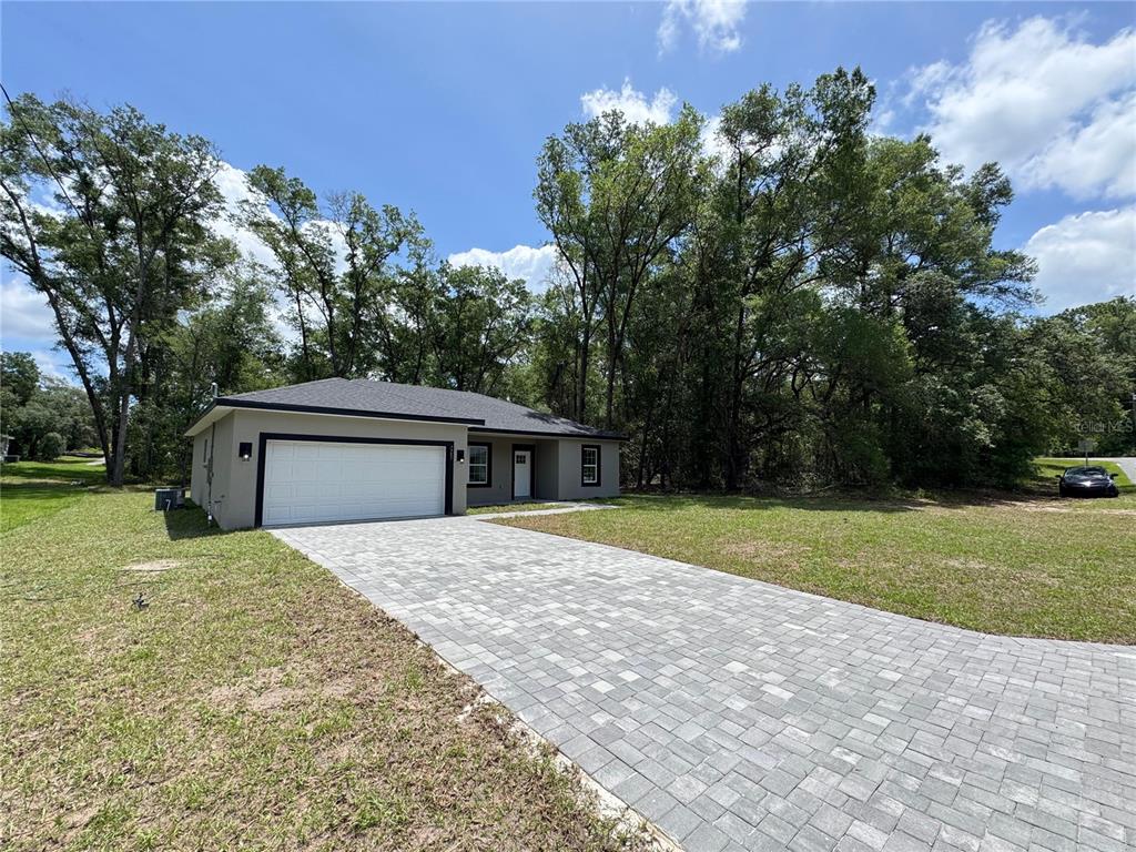 A single-story house with a white garage door and a paved driveway sits on a lawn — 7751 N CREEK WAY, CITRUS SPRINGS, FL