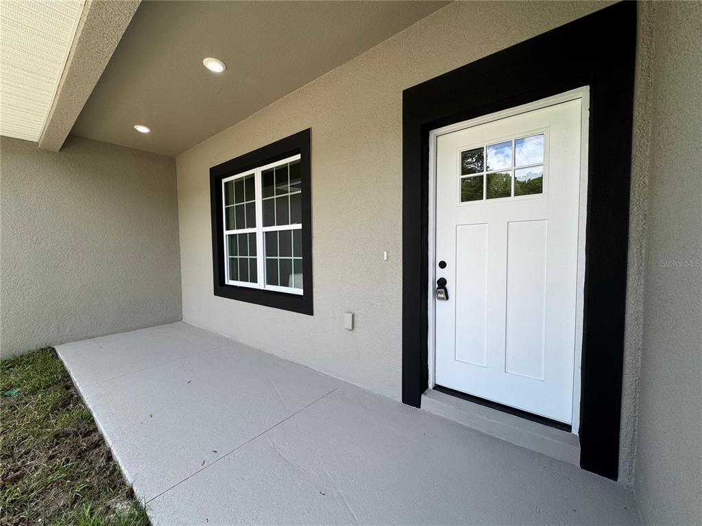 A covered concrete porch features a white front door and a window with black trim — 7751 N CREEK WAY, CITRUS SPRINGS, FL