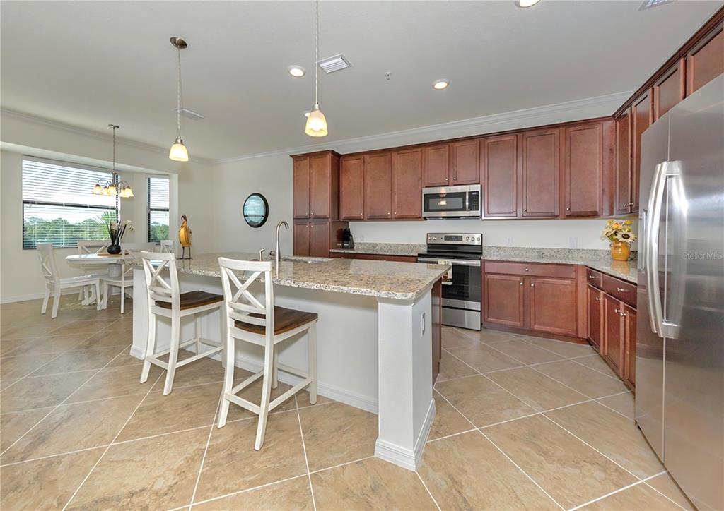 A kitchen with wood cabinets, granite countertops, a center island, and tile flooring — 17006 VARDON TERRACE UNIT 402, BRADENTON, FL