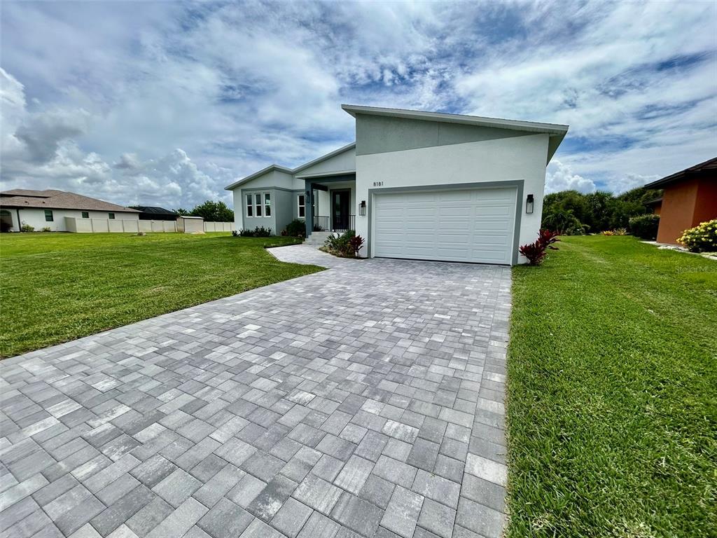 A modern single-story house features a paved driveway, a two-car garage, and a white exterior — 8181 TECUMSEH CIRCLE, PORT CHARLOTTE, FL