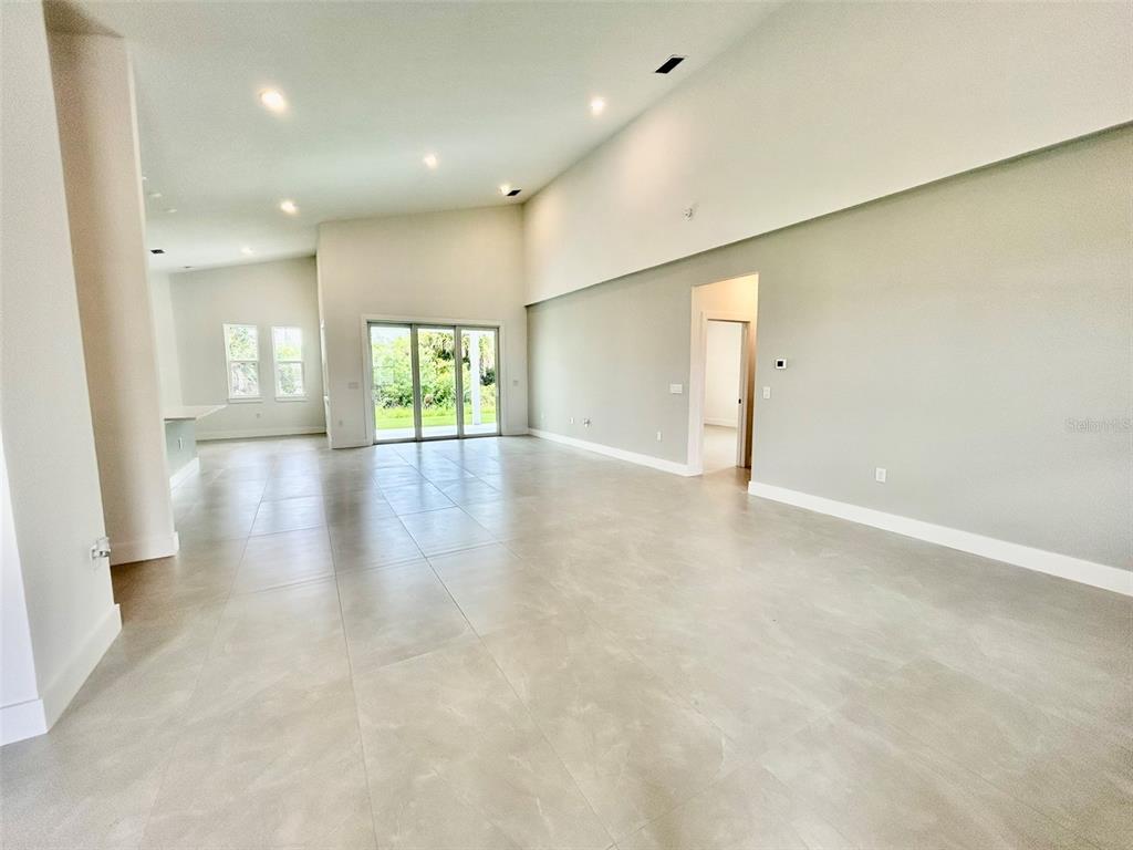 A spacious, open-concept living area features light-colored tile flooring, high ceilings, and sliding glass doors — 8181 TECUMSEH CIRCLE, PORT CHARLOTTE, FL