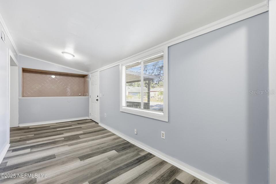 A room with light blue walls, wood-look flooring, a window, and a pass-through opening — 3428 GLEN STREET, JACKSONVILLE, FL
